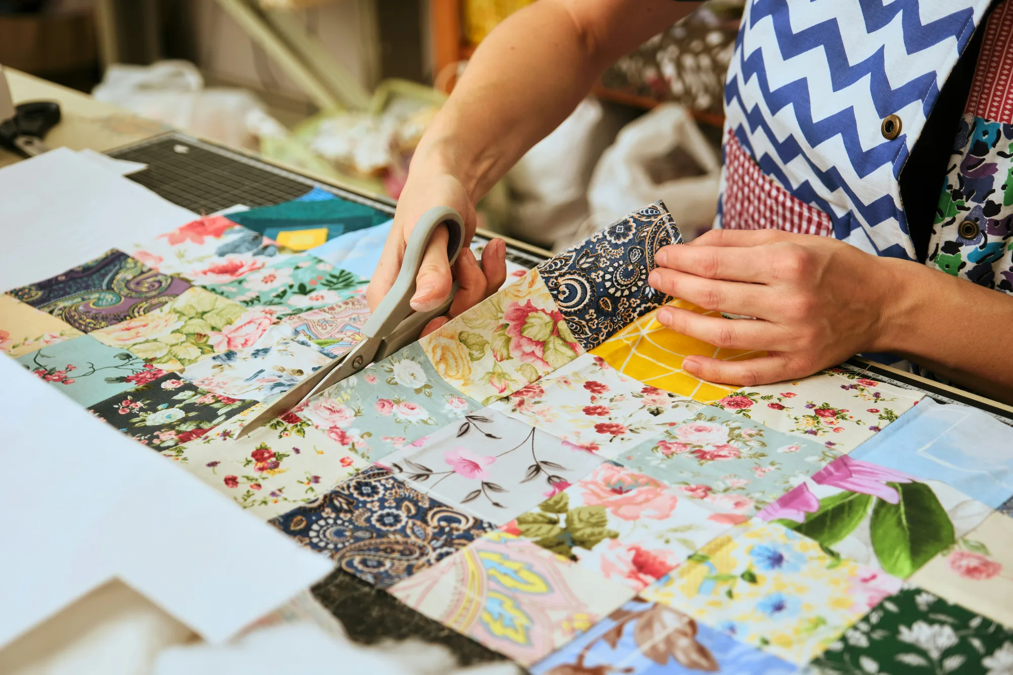 Hands cutting colourful patchwork fabric with scissors at a quilting class