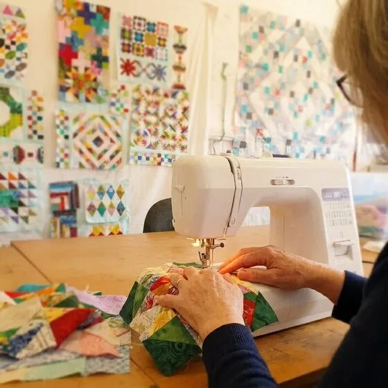 Hands guiding patchwork fabric through a sewing machine